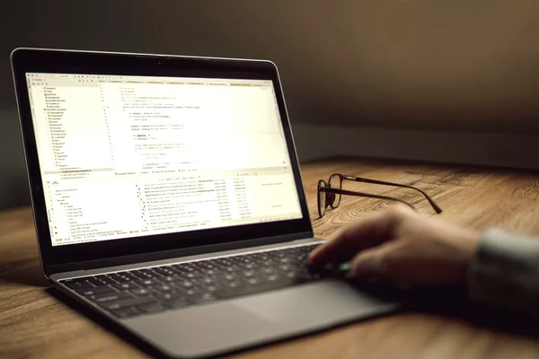 Ordinateur portable ouvert sur du code, posé sur un bureau en bois